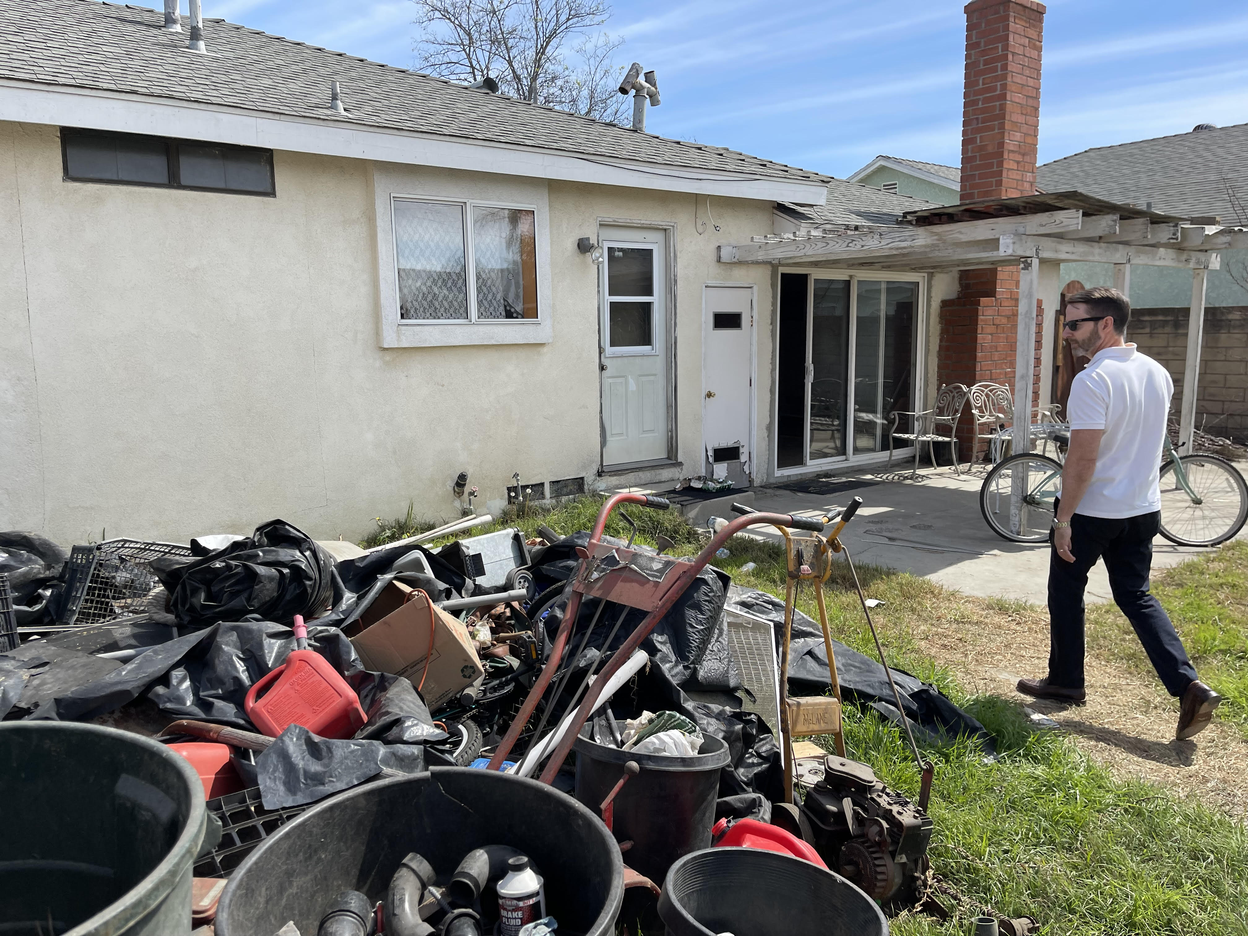 Eric Nerhood walking through the cluttered backyard of a property